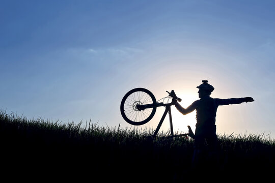silhouette of a cyclist with a bike in the grass in the sun.