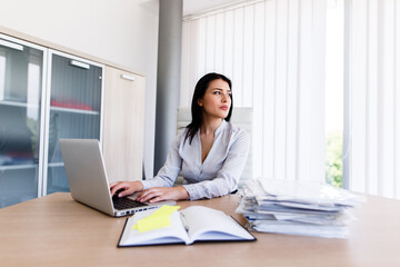 Attractive businesswoman looking trhougt window of her office while shes typing on laptop