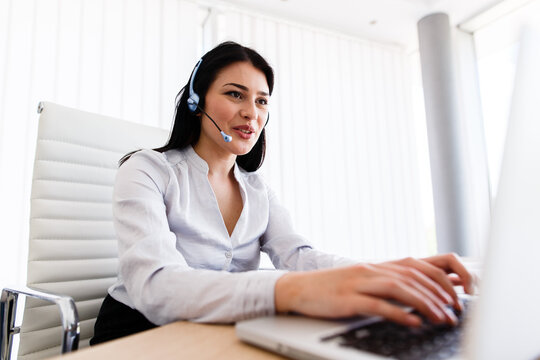 Attractive woman talking with customer at her work desk with headset