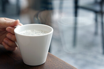 Hand holding cup of hot soy milk with basil seed on wooden table and copy space, Morning Breakfast, Healthy Drink Concept.