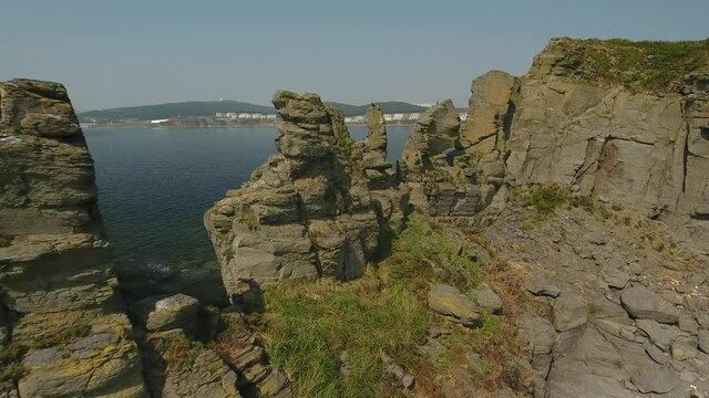 Green Standing rocks Kekura in the sea ocean. Patrokl peninsula Vladivostok Primorsky krai nature. Russky bridge at background.  Aerial drone flight close to clif. Summer day clear. 4k
