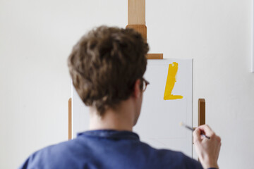 artist seen from the back painting yellow paint on a white canvas