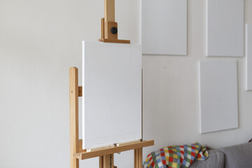 an empty canvas on an easel with multiple empty canvasses on the wall behind