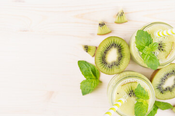Green kiwi fruit smoothie in glass jars with straw, mint leaf, cute ripe berry, top view. White wooden board background, decorative border, copy space.