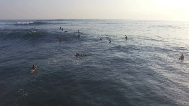 Drone shot of surfers paddling out to ocean and trying to catch waves at beautiful summer day in Bali