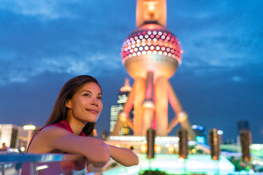 Shanghai city urban travel Asian woman tourist. Multiracial girl relaxing enjoying looking at city lights at night in Pudong, Shanghai, China with chinese landmark. Multicultural young professional.