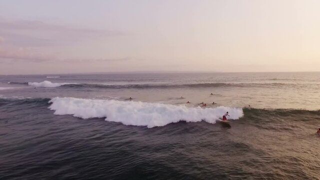 Drone shot of surfers riding waves in ocean at beautiful sunrise in Bali