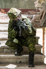 Portrait of armed woman with camouflage. Young female soldier observe with firearm. Child soldier with gun in war hearth, house ruins background.  Military, army people concept