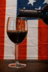 Red wine pouring into wine glass with American flag background.