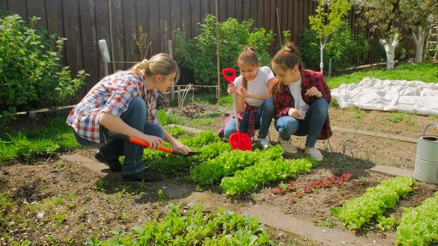 4K footage of young woman teaching her daughters how to plant at garden