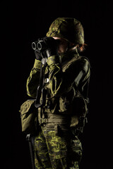 Portrait of armed woman with camouflage. Young female soldier observe with binoculars. Child soldier with gun in war, black background.  Military, army people concept