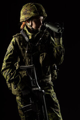 Fototapeta premium Portrait of armed woman with camouflage. Young female soldier observe with binoculars. Child soldier with gun in war, hause ruins background. Military, army people concept