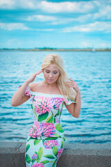 A beautiful european girl with a figure and the right features in a dress with a floral princess resting on the weekend enjoying the sun and a beautiful view of the water