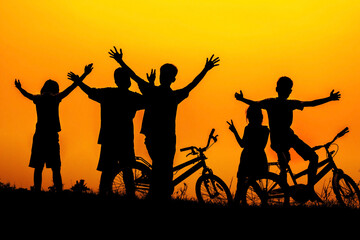 Boys and girls standing and sitting behind a bike with sunset Silhouette.