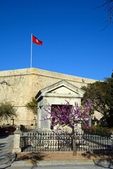 Maltese flag on top of St Johns Cavalier building with a memorial in the foreground in Hastings Gardens, Valletta, Malta.