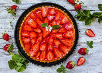 Delicious sponge cake with jelly and fresh strawberries on a wooden background.
