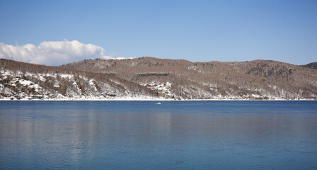 Obraz premium Baikal lake spring landscape view. Snow-covered shore of the lake. Rocky forested coastline.