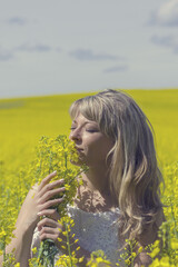 Beautiful dreamy woman in a rapeseed field with a bouquet dreams and enjoys nature.