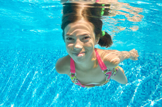 Child swims in pool underwater, happy active girl dives and has fun in water, kid fitness and sport on family vacation
