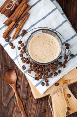 Glass Cup of hot coffee with foam, scattered grain, wooden brown background.Flat lay