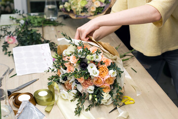 Woman have pack festive bouquet in wrapping paper. Young beautiful florist make floristry assemble...