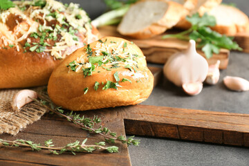 Tasty bun with grated cheese, garlic and herbs on cutting board