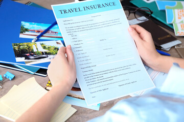 Woman sitting at workplace and holding blank travel insurance form, closeup