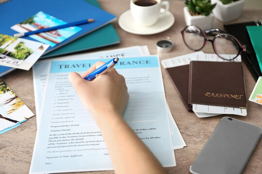 Woman filling in blank travel insurance form on table