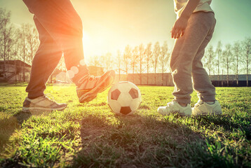Father and son playing together with ball in football under sun