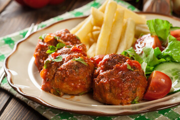 Roasted meatballs in tomato sauce with french fries and salad