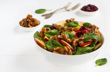 Healthy vegetarian salad with green spinach leaves, dried cranberry, red apple and walnuts caramelized in honey in a white bowl on the wooden table. - 157374240