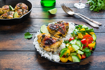 Healthy balanced dinner, spicy and crispy homemade cilantro lime chicken thighs, rice and salad with fresh vegetables.