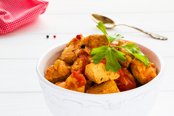 Healthy low-calorie dish, chicken fillet stewed with vegetables, in a white bowl on the wooden table, closeup.