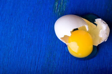 Chicken eggs on blue wooden background. Top view. Broken egg. Copy space.