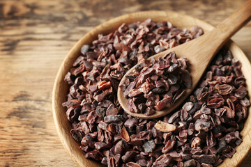 Wooden bowl and spoon with cocoa nibs on table