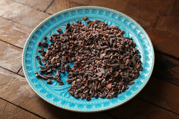 Plate with cocoa nibs on wooden table