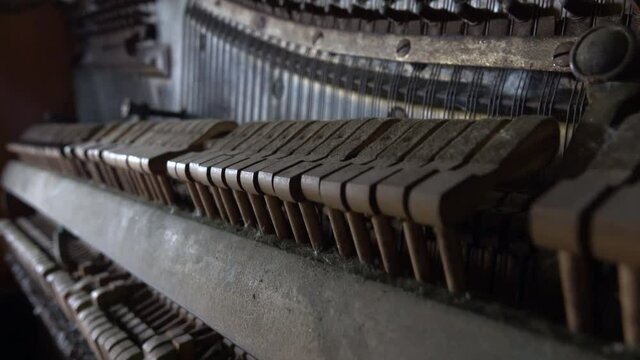 CLOSE UP, DOF: Old broken dusty piano from the inside. Hammers in abandoned piano striking strings tuned to produce the note when a piano key is pressed. Music playing from the ancient ruined piano