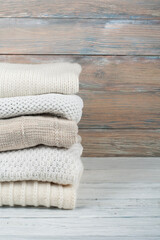 Fototapeta na wymiar Knitted wool sweaters. Pile of knitted winter clothes on wooden background, sweaters, knitwear, space for text.