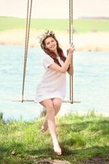 Beautiful young woman on swing near river