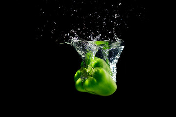 Green peppers splashing water on black background