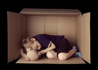 Poor little girl sleeping in cardboard box on black background
