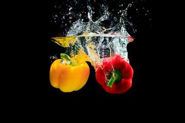 Yellow and red pepper splashing water on black background