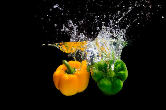 Yellow and green peppers splashing water on black background