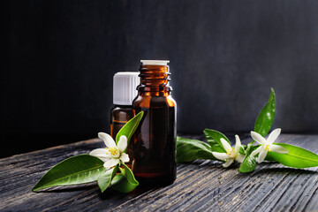 Neroli (Citrus aurantium) essential oil in a brown glass bottle with fresh white flowers on old...