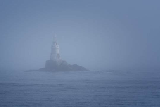 Fototapeta Lighthouse Along Rocky Coastline on Foggy Morning