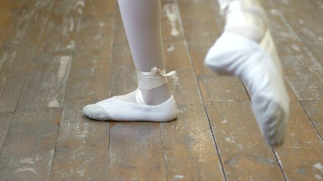 Close-up of a girl's legs in white ballet shoes on an old wooden floor during ballet training. Element of classical dance exercise.