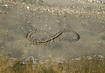 The sign of infinity on the sea. Coastal sand on the beach. The symbol of infinity