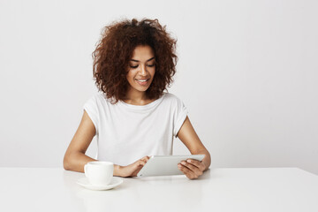 Beautiful african girl smiling looking at tablet over white background. Copy space.