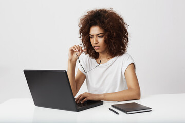African businesswoman looking at laptop screen thinking over white background.