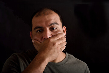 Man covering his mouth on black background
